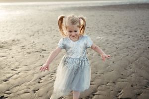 Small figure twirling in a light blue dress on sandy beach at sunset.