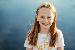 Portrait of a smiling youth with long hair against blue sky background.