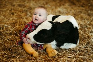 Baby explores and interacts with friendly black and white farm cat on hay bales.
