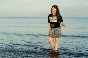 Person wearing graphic t-shirt and skirt wading in shallow ocean water at dusk.