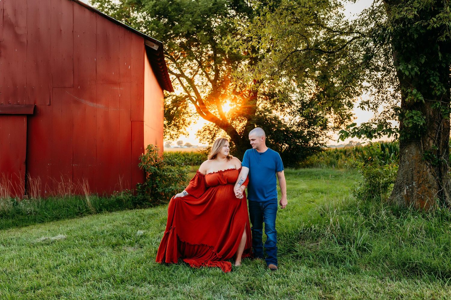 A family portrait beside a red barn with sunlight streaming through trees.