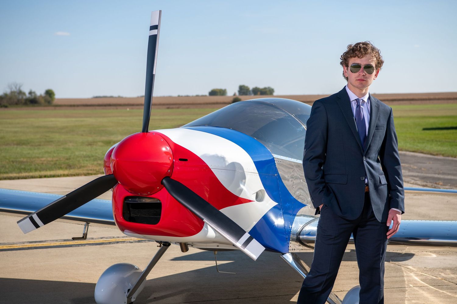 Professional in suit poses confidently beside red and white aircraft on airfield.