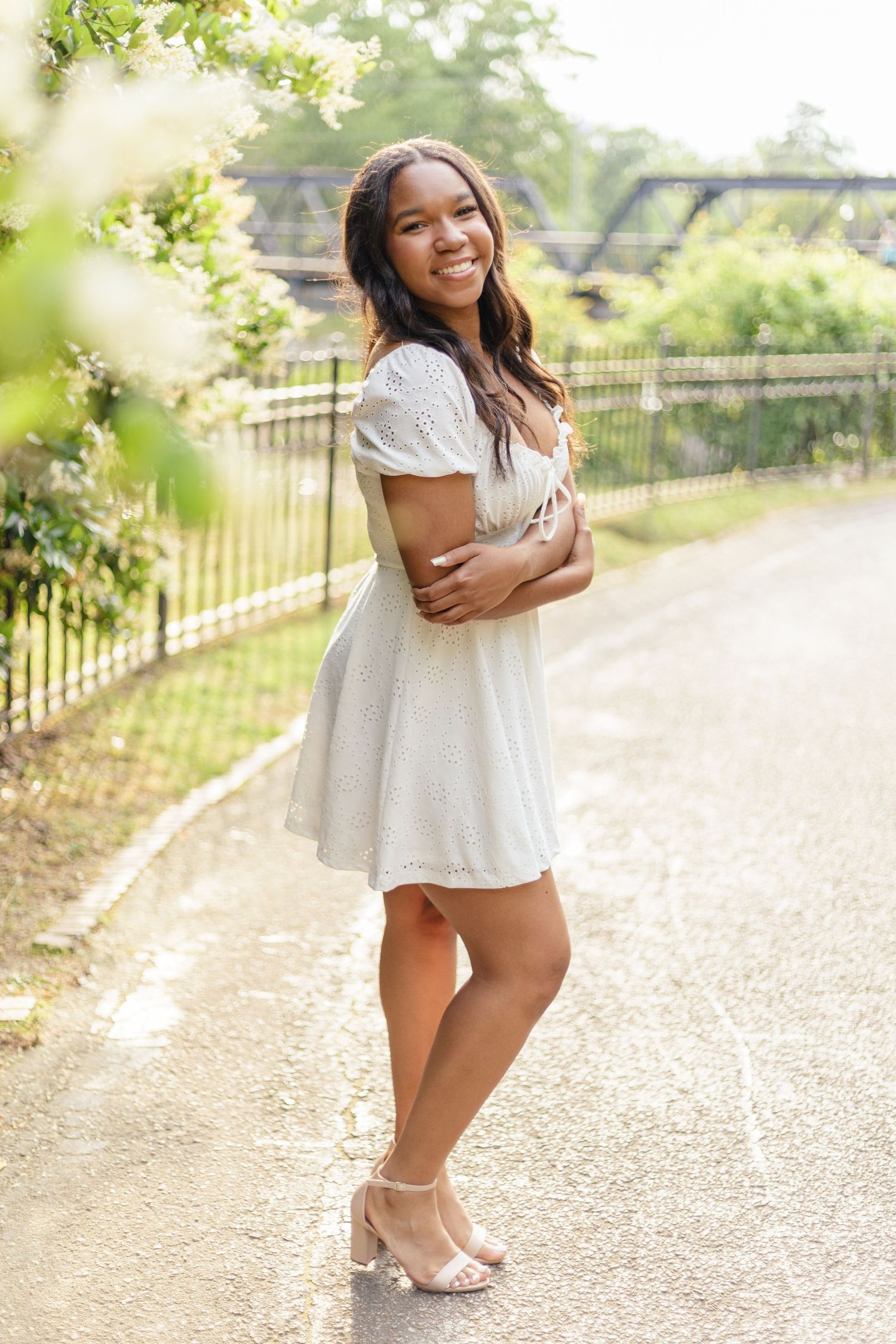 Portrait in white dress against garden backdrop with joyful expression.