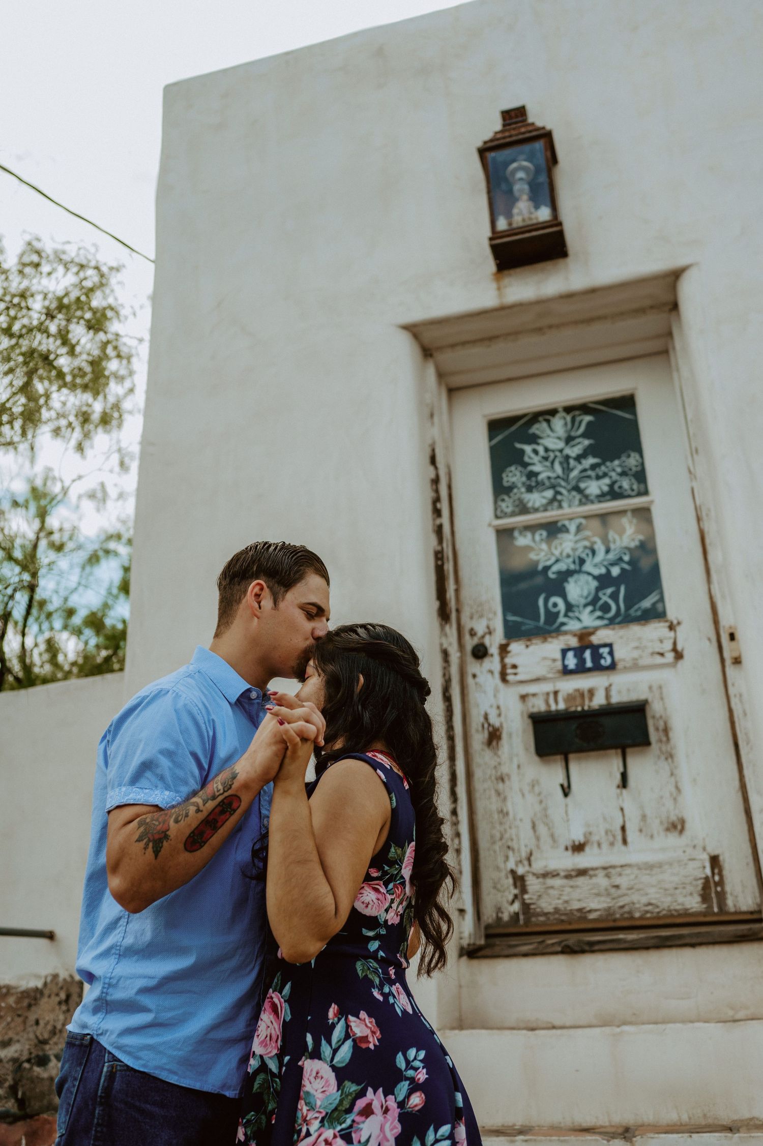 A couple shares tender moments outside a white stucco building with vintage windows.