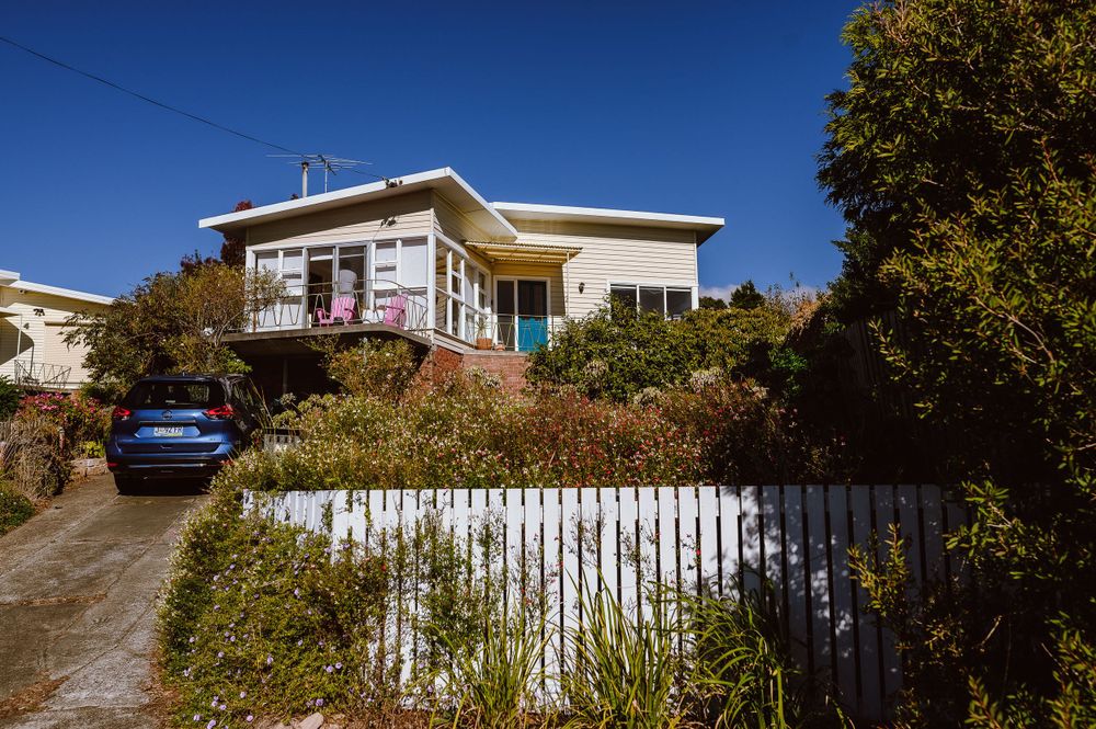 A charming hillside house with turquoise door and white picket fence on a sunny day.