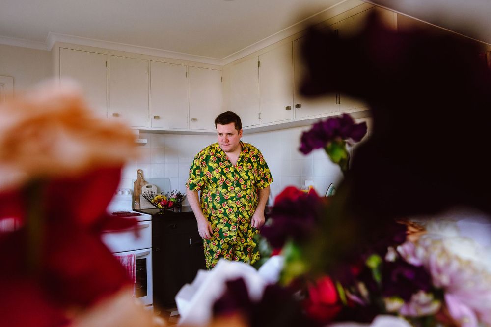 A person in a floral print outfit stands in a kitchen with flowers in the foreground.