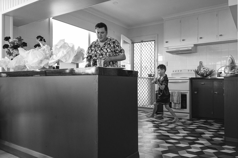A black and white photo showing people in a modern kitchen with checkered flooring and white cabinets.