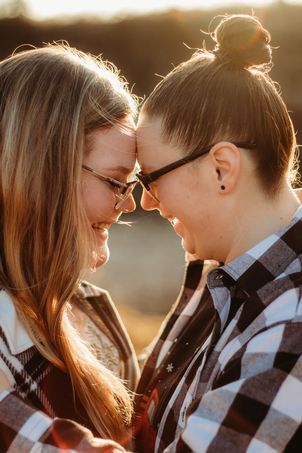 A couple resting foreheads smiling at each other and the sun is glowing behind them.