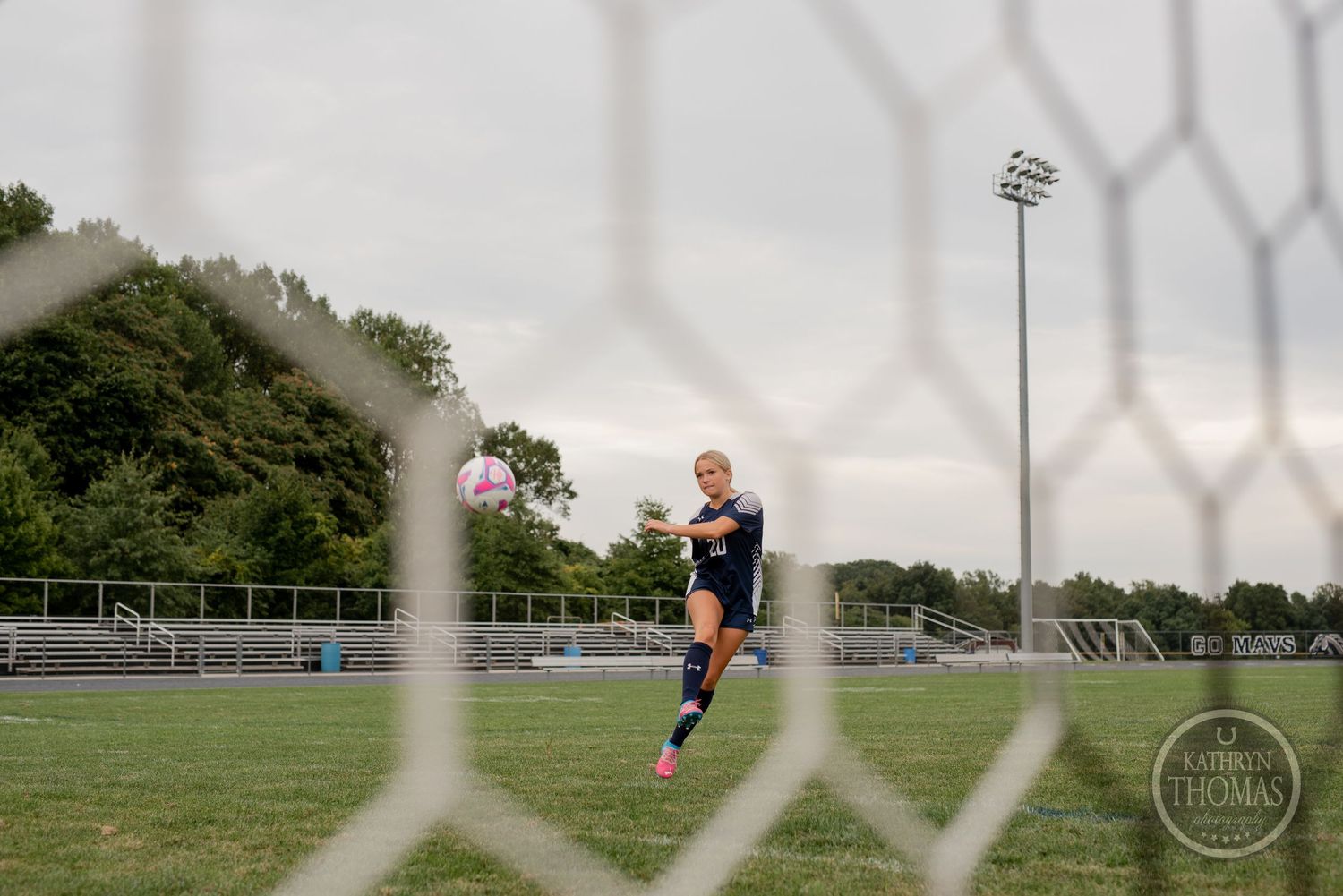 Soccer player running on field viewed through goal net with stadium lights in background.