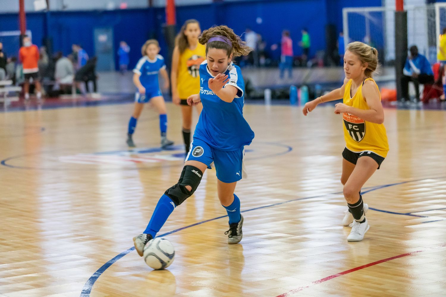 Youth athletes playing indoor futsal on blue court surface.