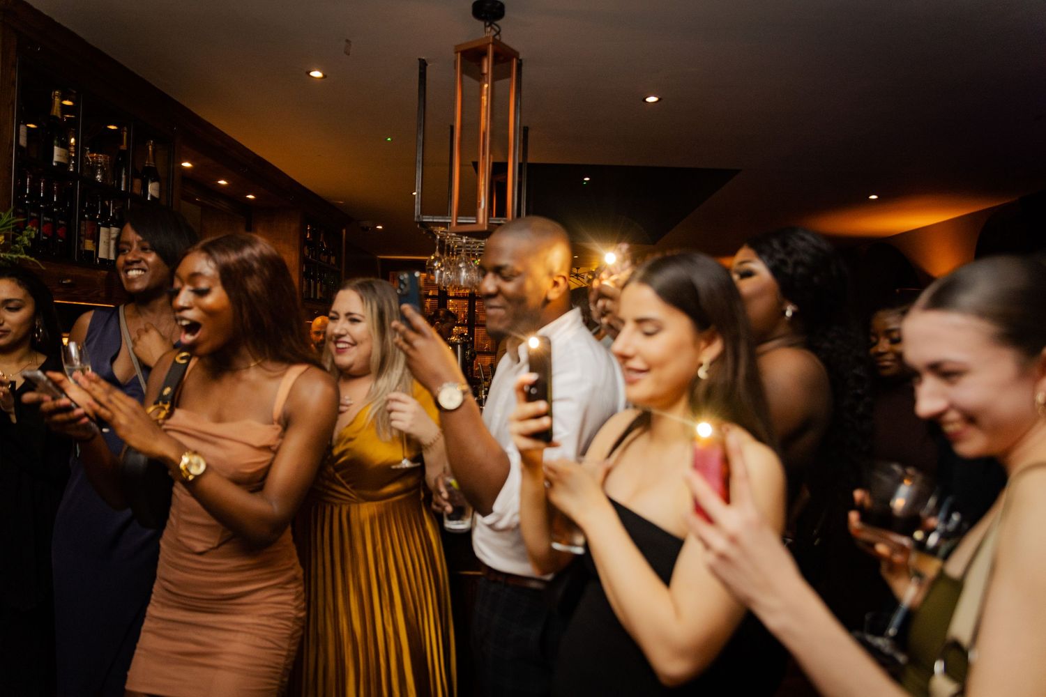 A group of partygoers dancing and clapping together in a dimly lit venue.