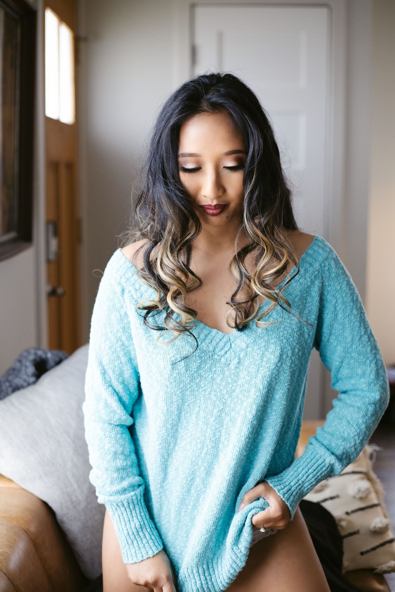 Lei on the kneeling on couch with only her aqua sweater