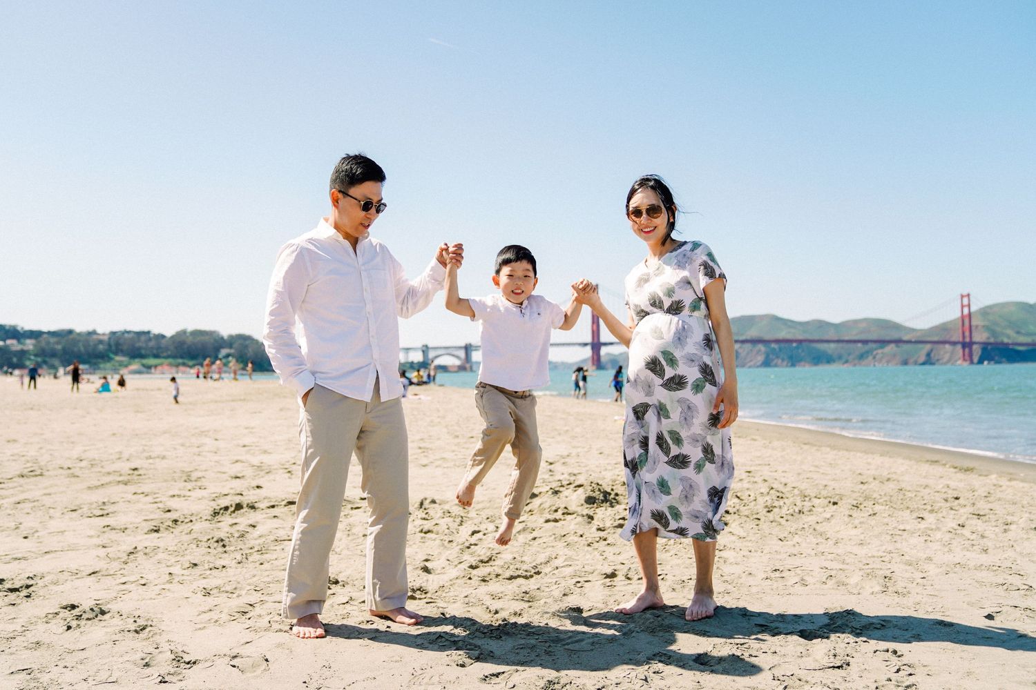 Family enjoying playful moment together on sandy beach with Golden Gate Bridge in background.