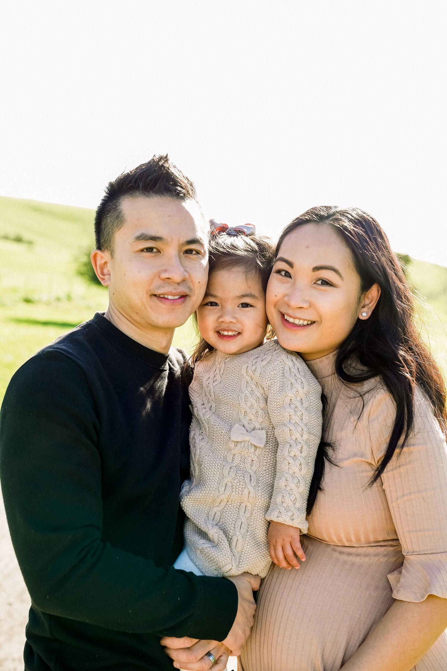 Family portrait in natural sunlight against green rolling hills background.