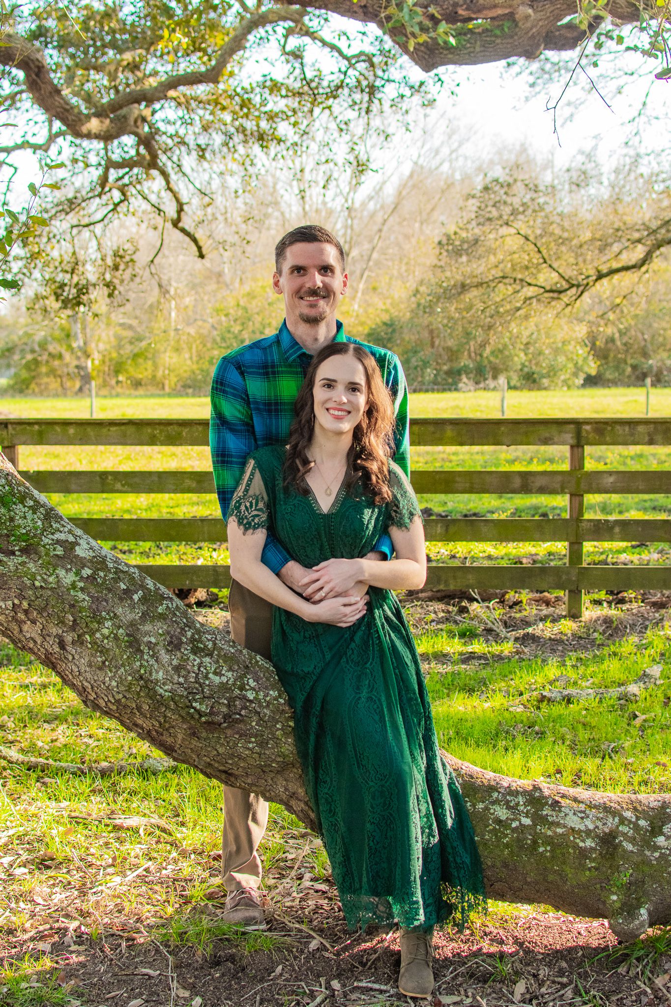 A couple poses together by a large tree branch in coordinating green attire.