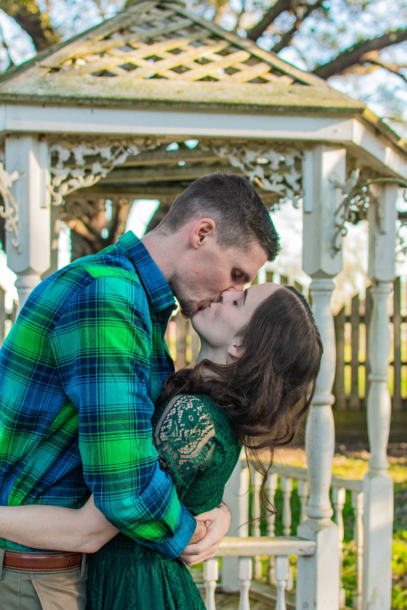 A romantic moment shared under a decorative white gazebo surrounded by trees.