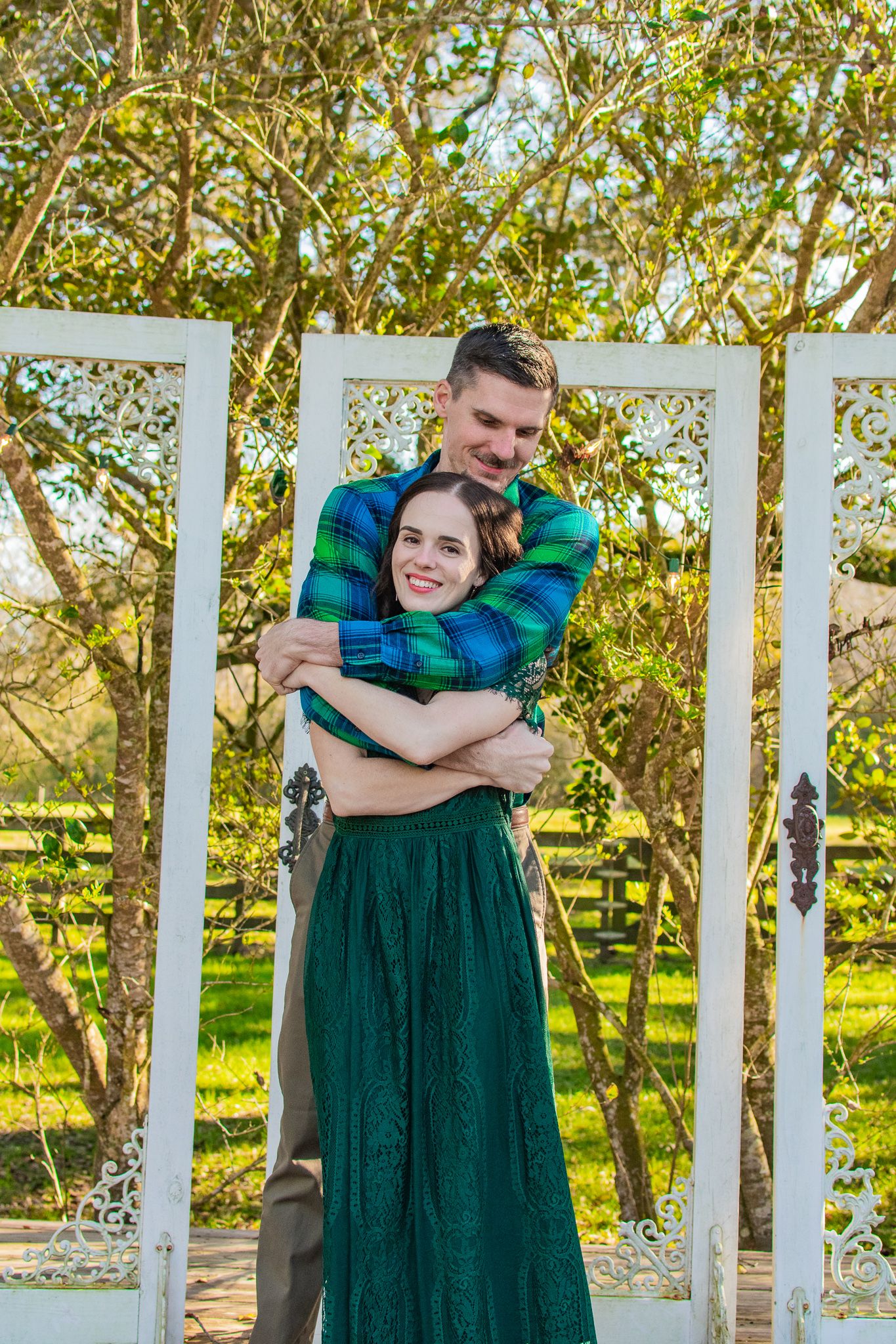Couple embracing in coordinated green outfits against white gazebo and garden setting.