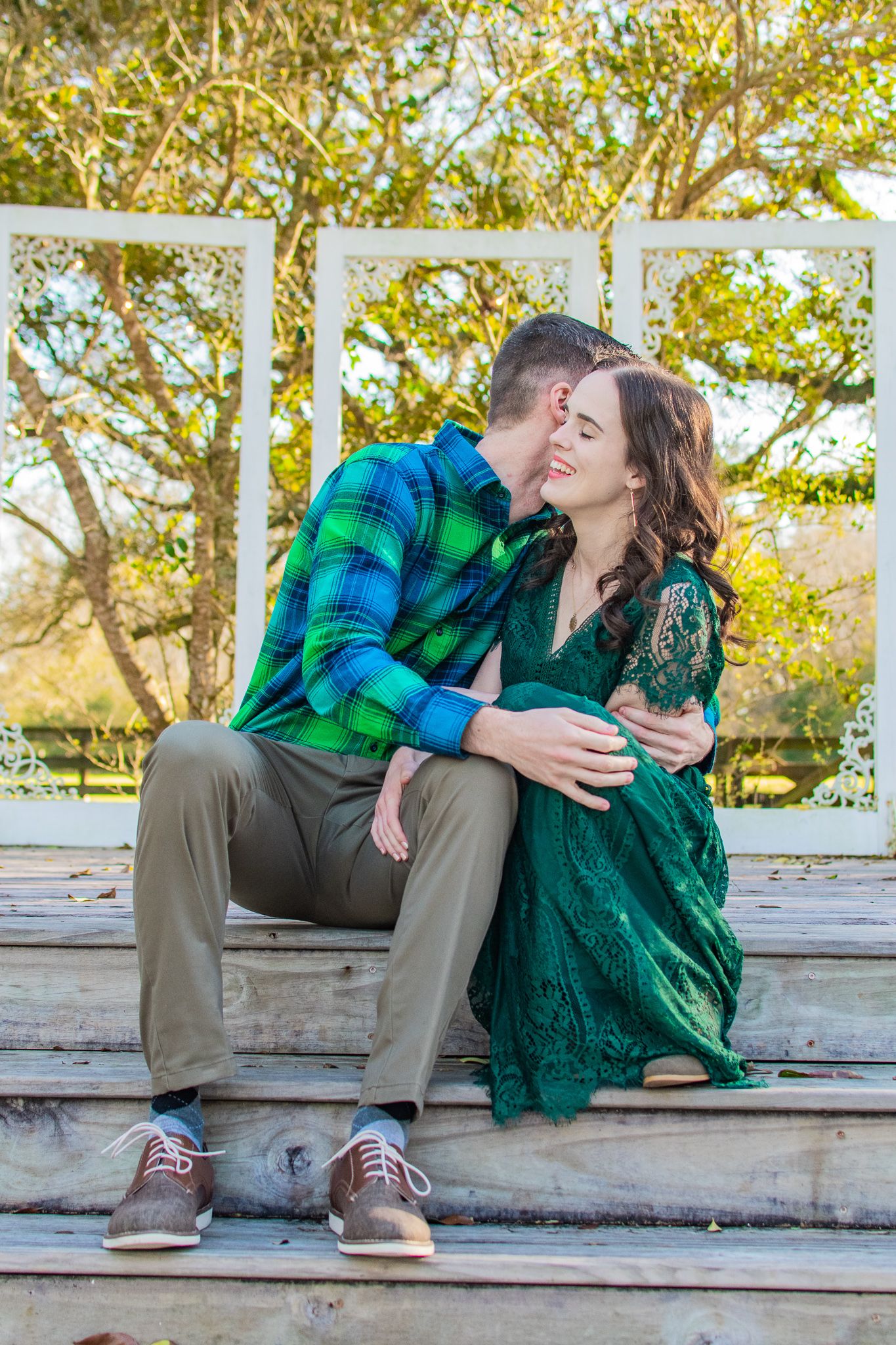 Couple in green sharing intimate moment on gazebo steps surrounded by trees.