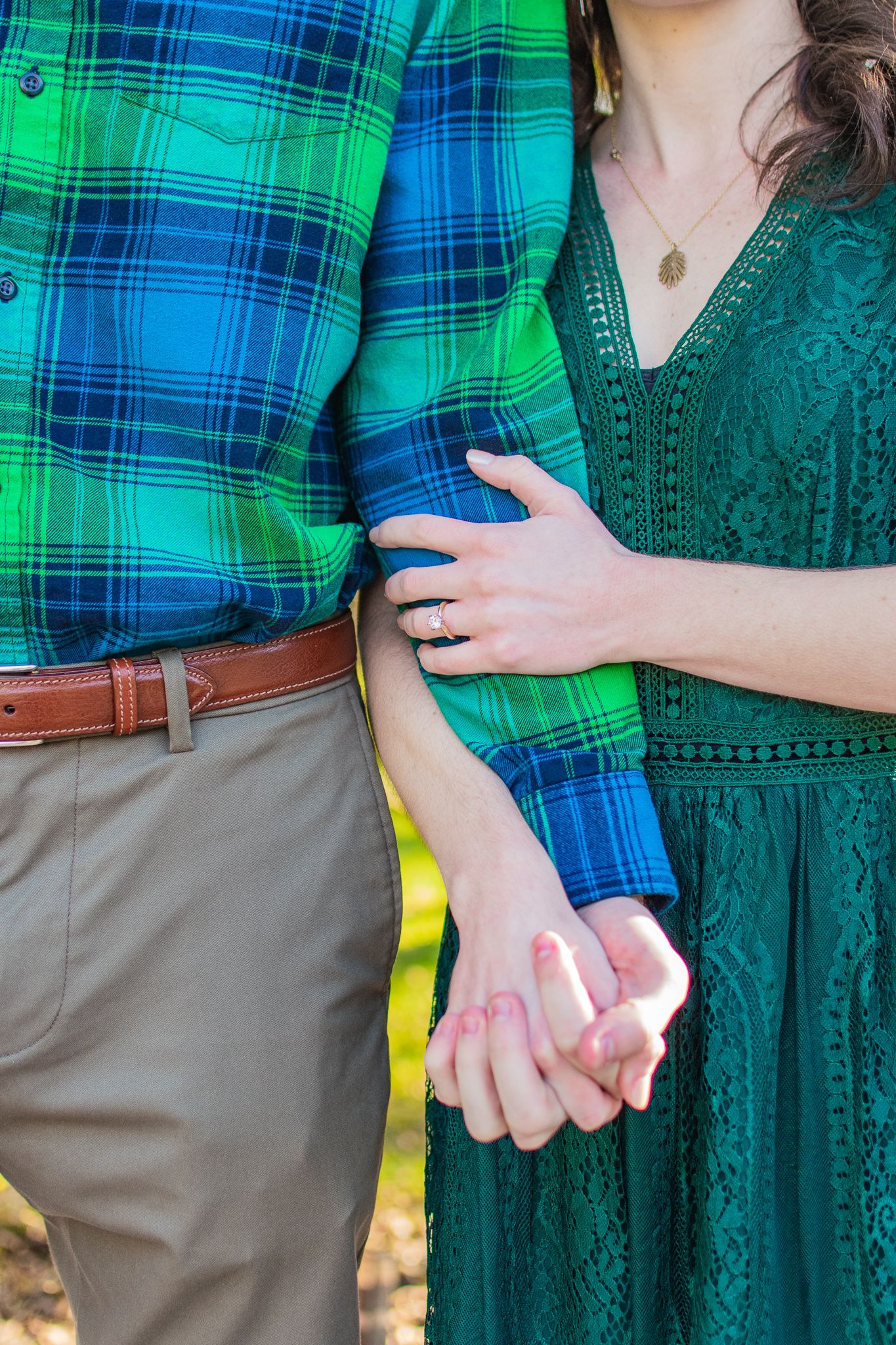 Close up of couple holding hands wearing coordinating green plaid and emerald lace clothing.