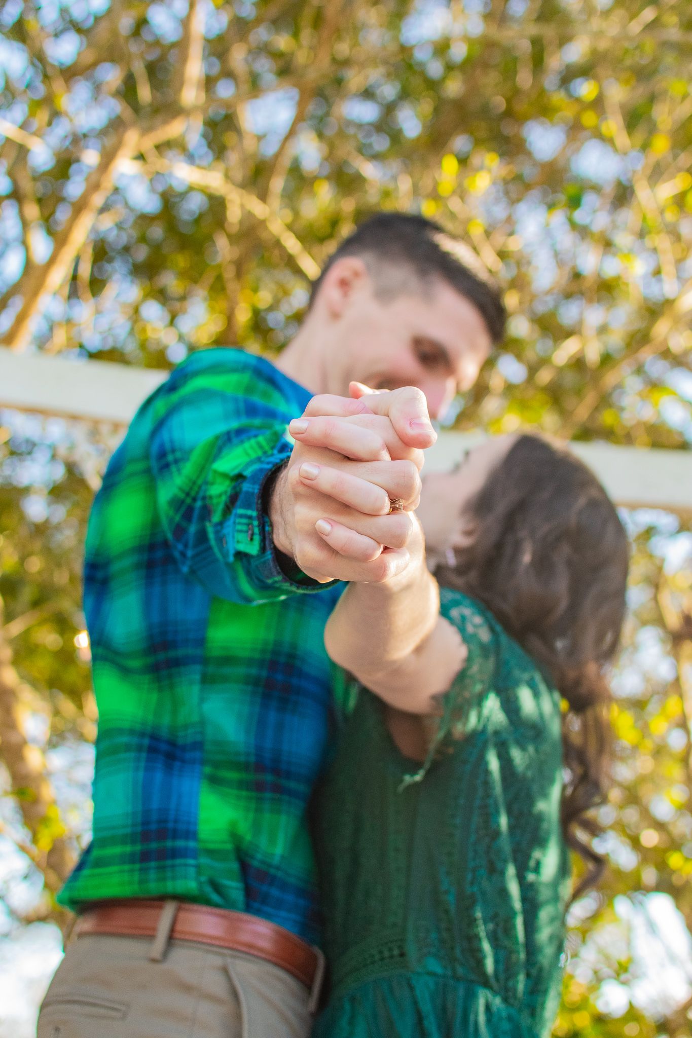 Dancing couple in coordinated green outfits holding hands against sunny garden backdrop.