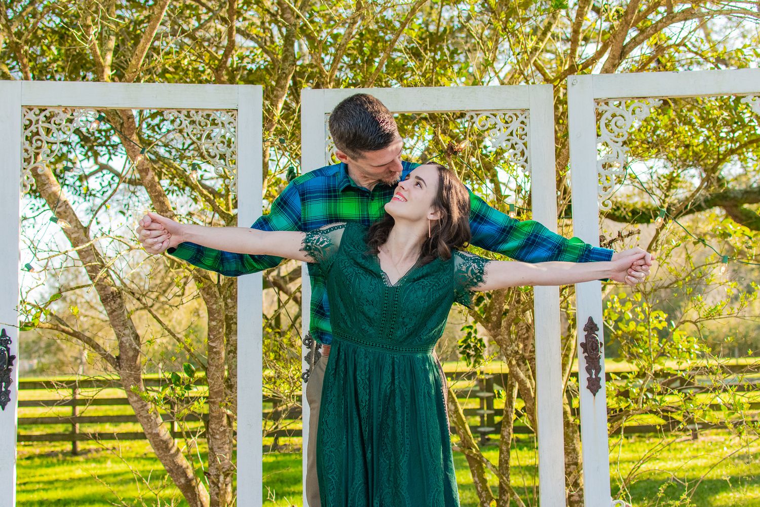 Couple in matching green outfits sharing playful dance moment in white gazebo.