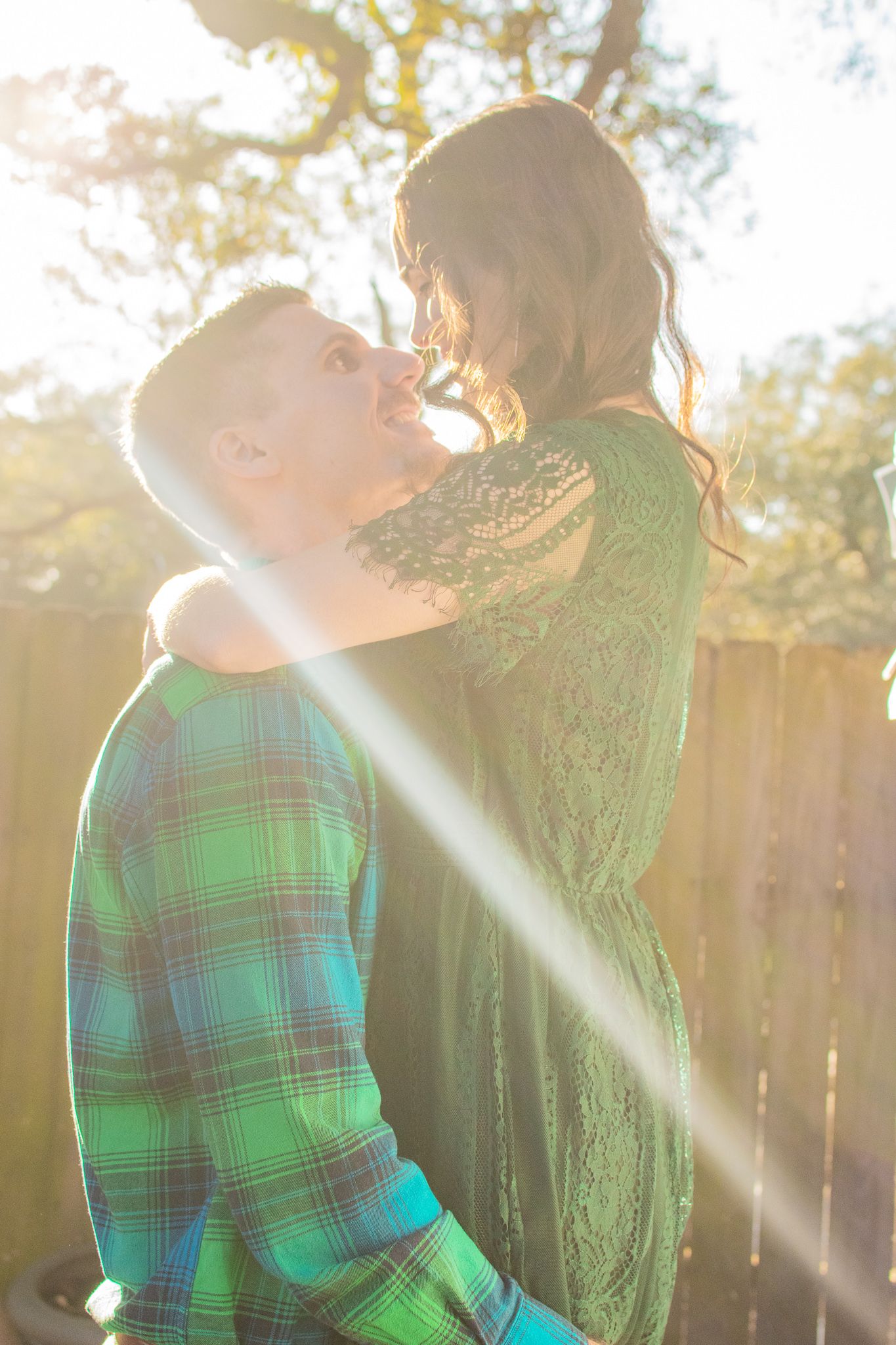 Couple embracing in sunlit outdoor setting wearing matching green attire.