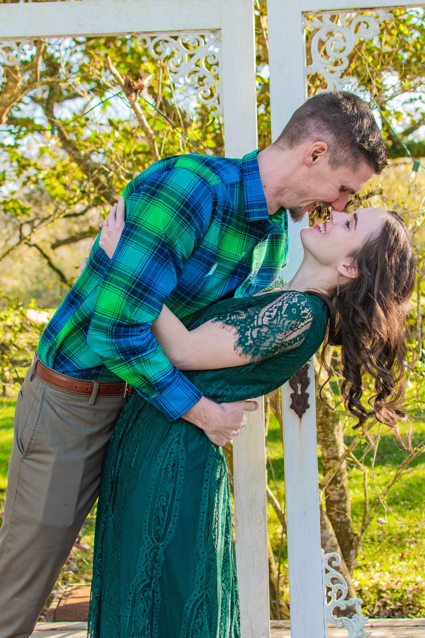 Romantic moment between couple wearing green plaid and emerald dress by white gazebo.