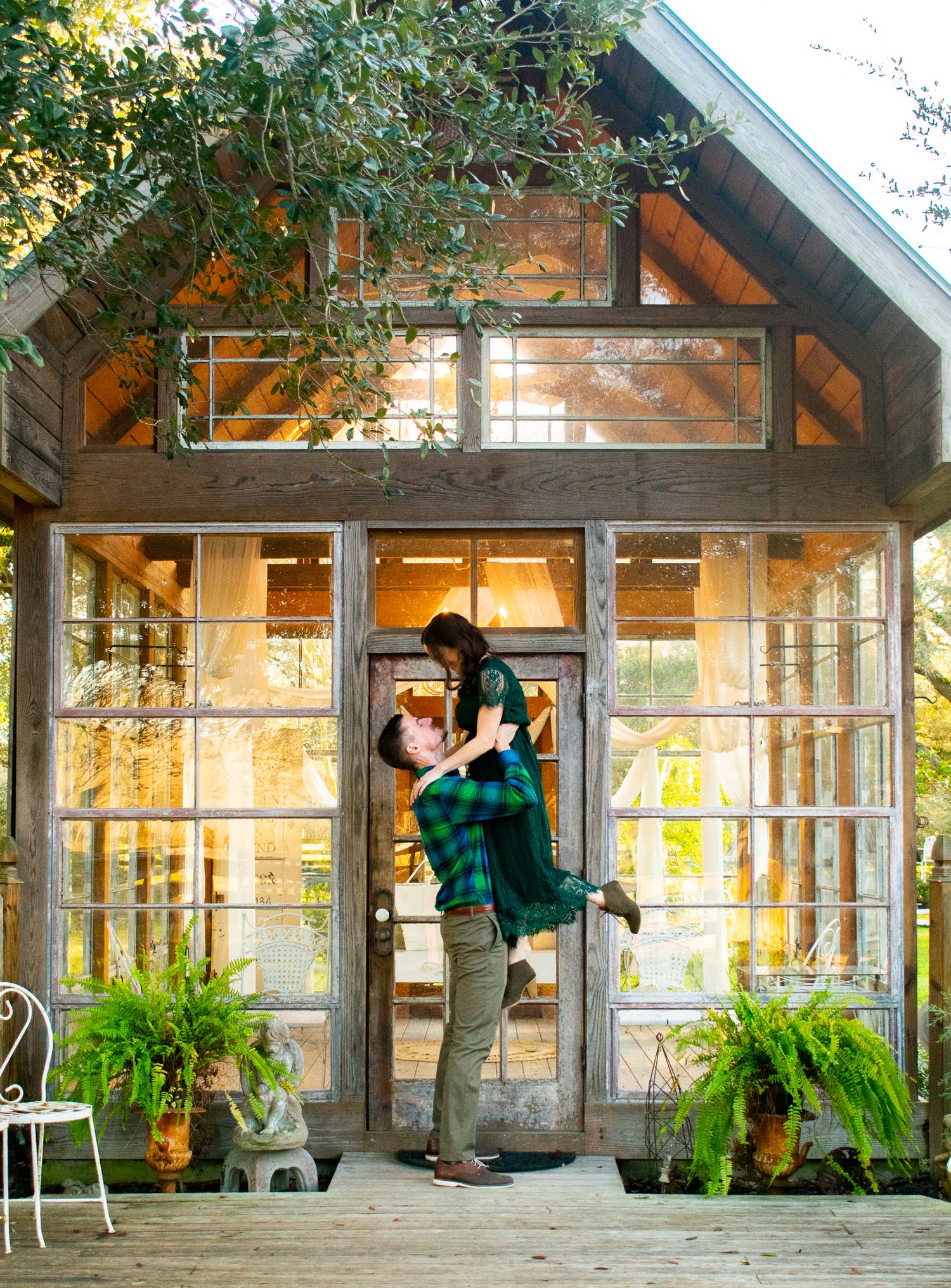 Couple sharing romantic moment in front of rustic glass house with plants.