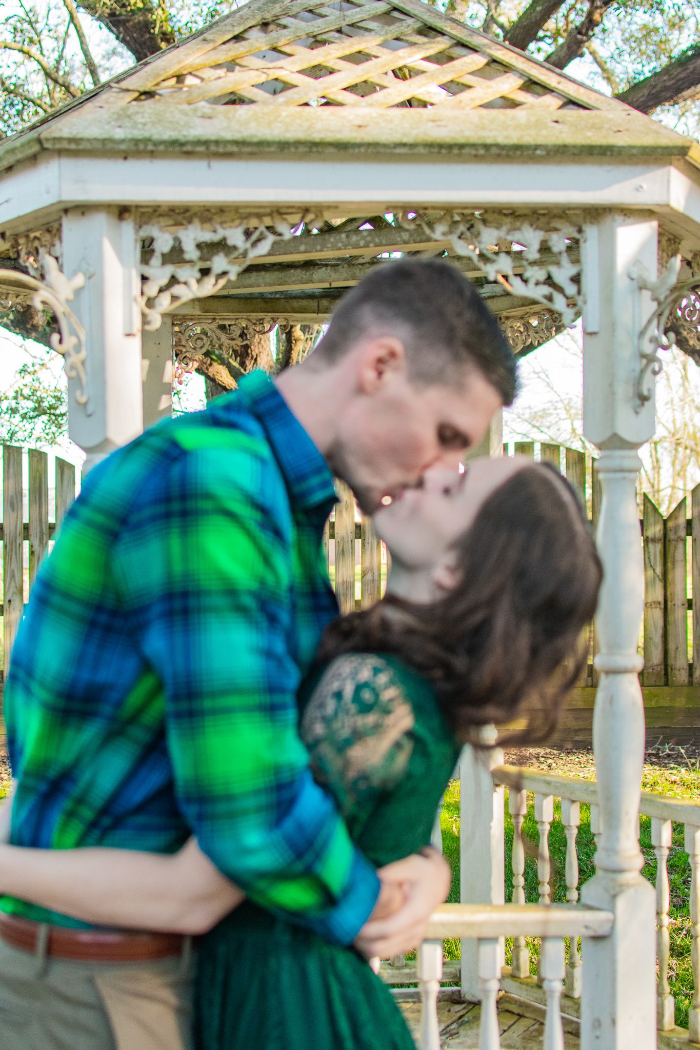 A tender kiss captured under an ornate white gazebo on a sunny day.