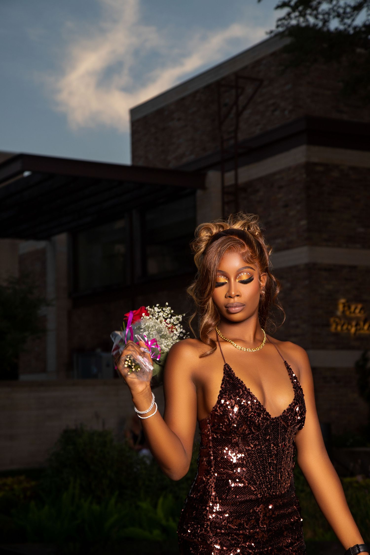 Evening portrait in sequined dress holding flowers at sunset.
