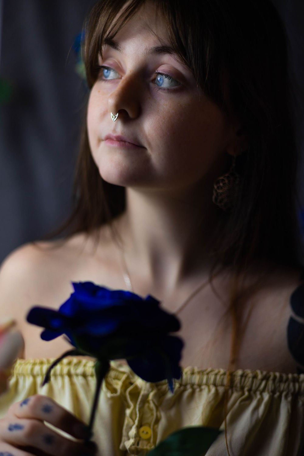 Dramatic portrait with blue flowers and off-shoulder yellow garment in low light.
