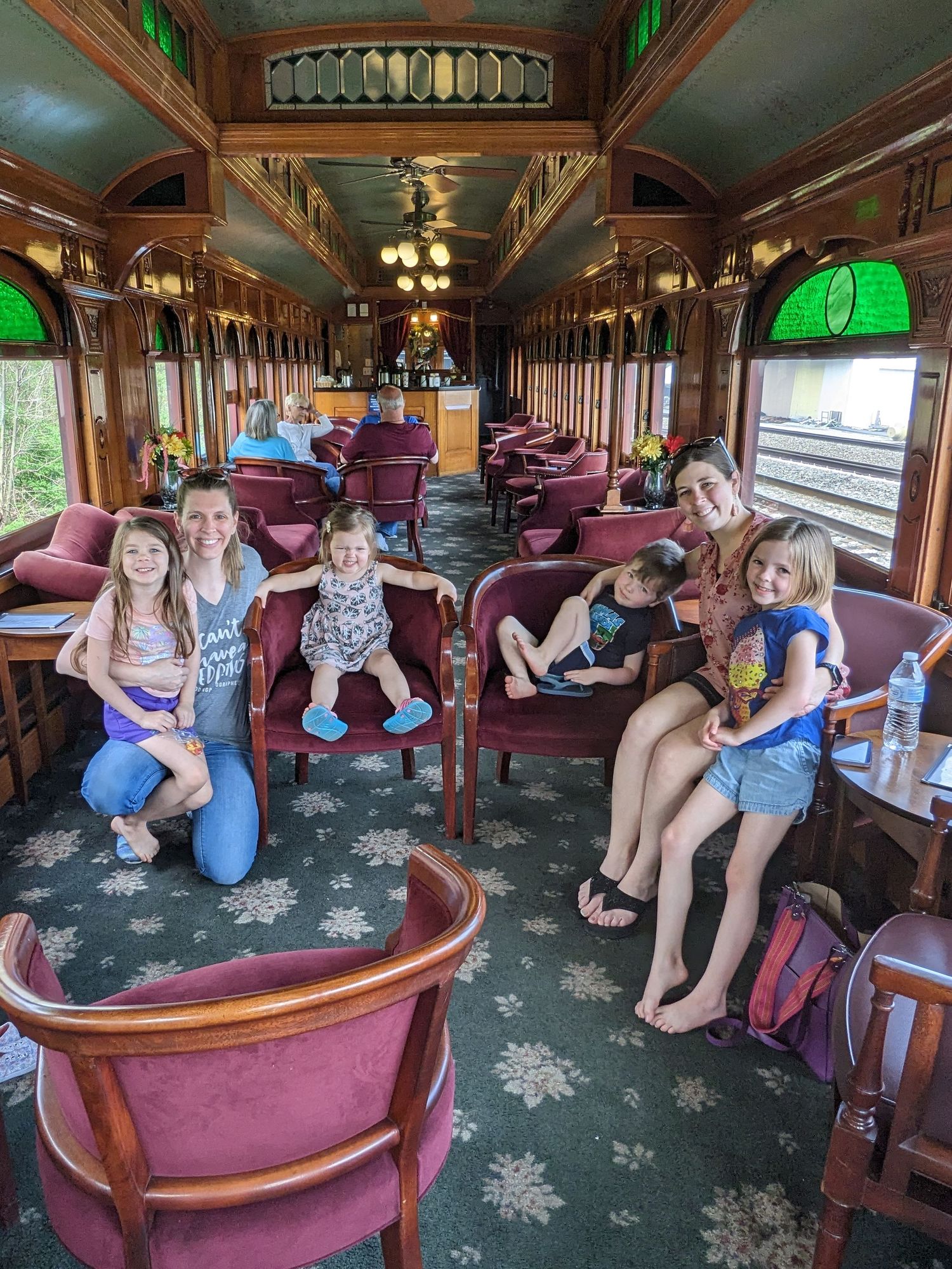 Interior of vintage train car with plush burgundy seating and green stained glass windows.