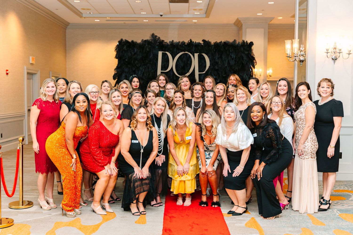 Large group photo of formally dressed people at red carpet event with POP backdrop.