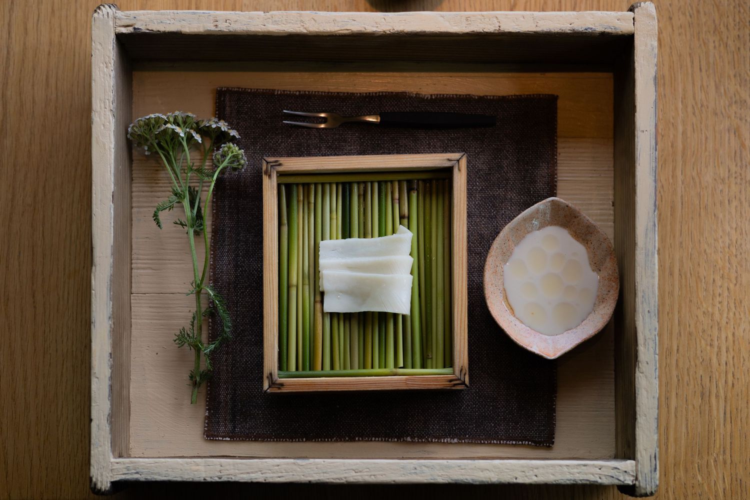 Minimalist table setting with bamboo placemat and decorative plate in wooden box frame.