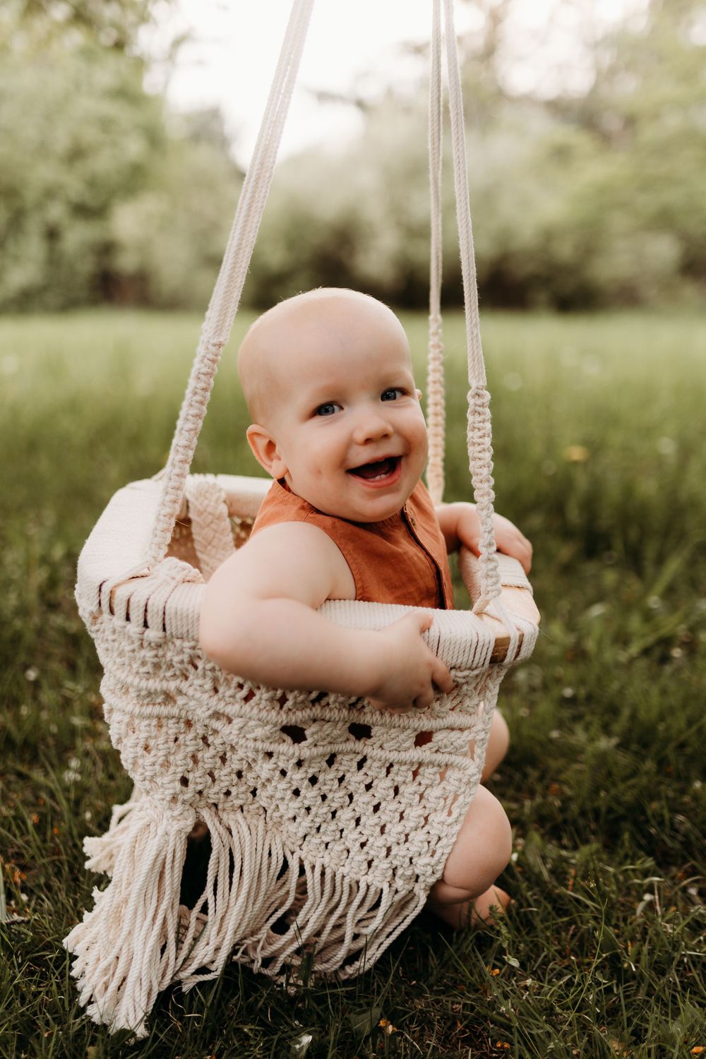 Joyful baby laughing while sitting in macrame swing outdoors.