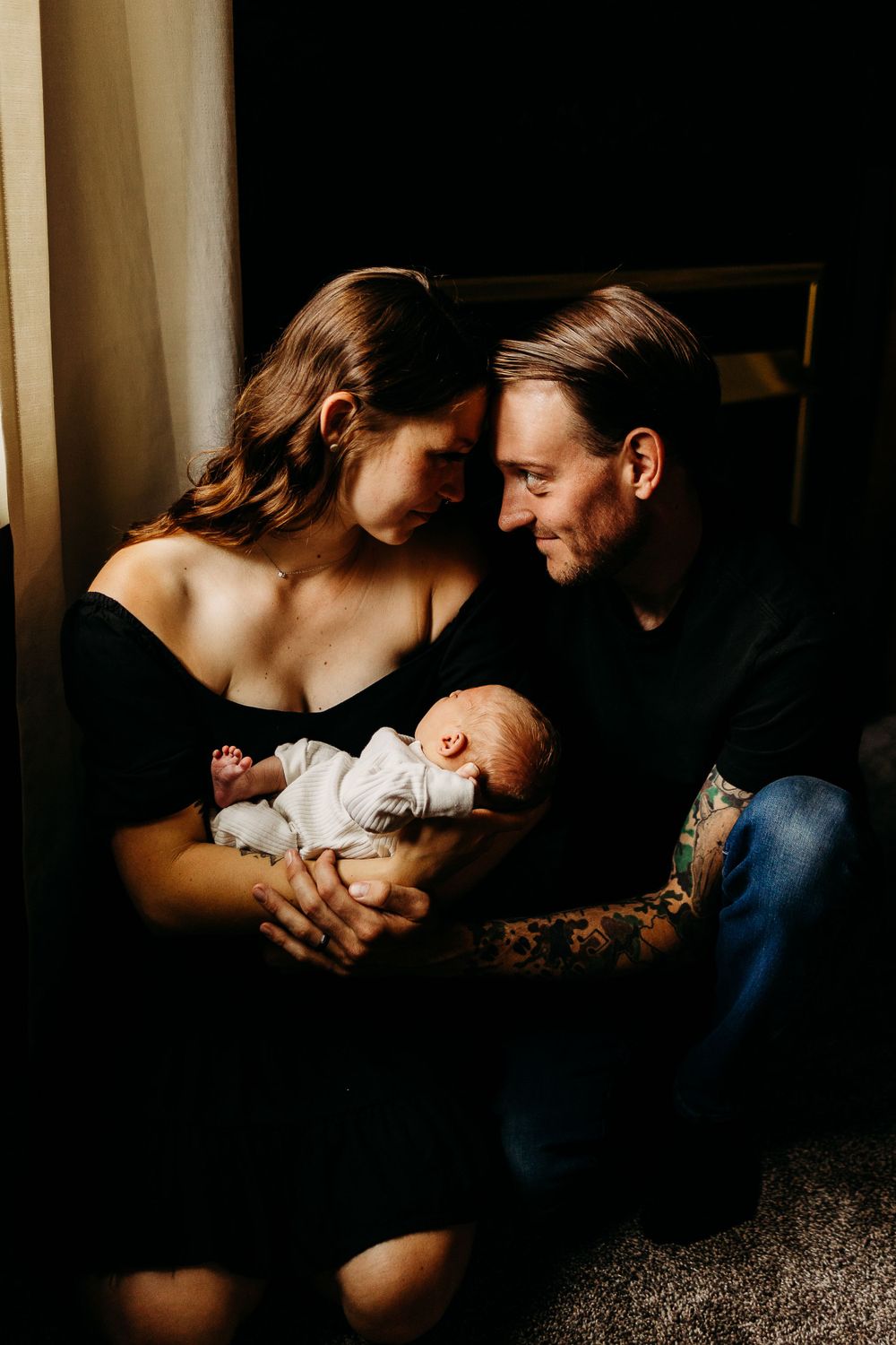 Intimate family moment in moody window light with newborn baby.