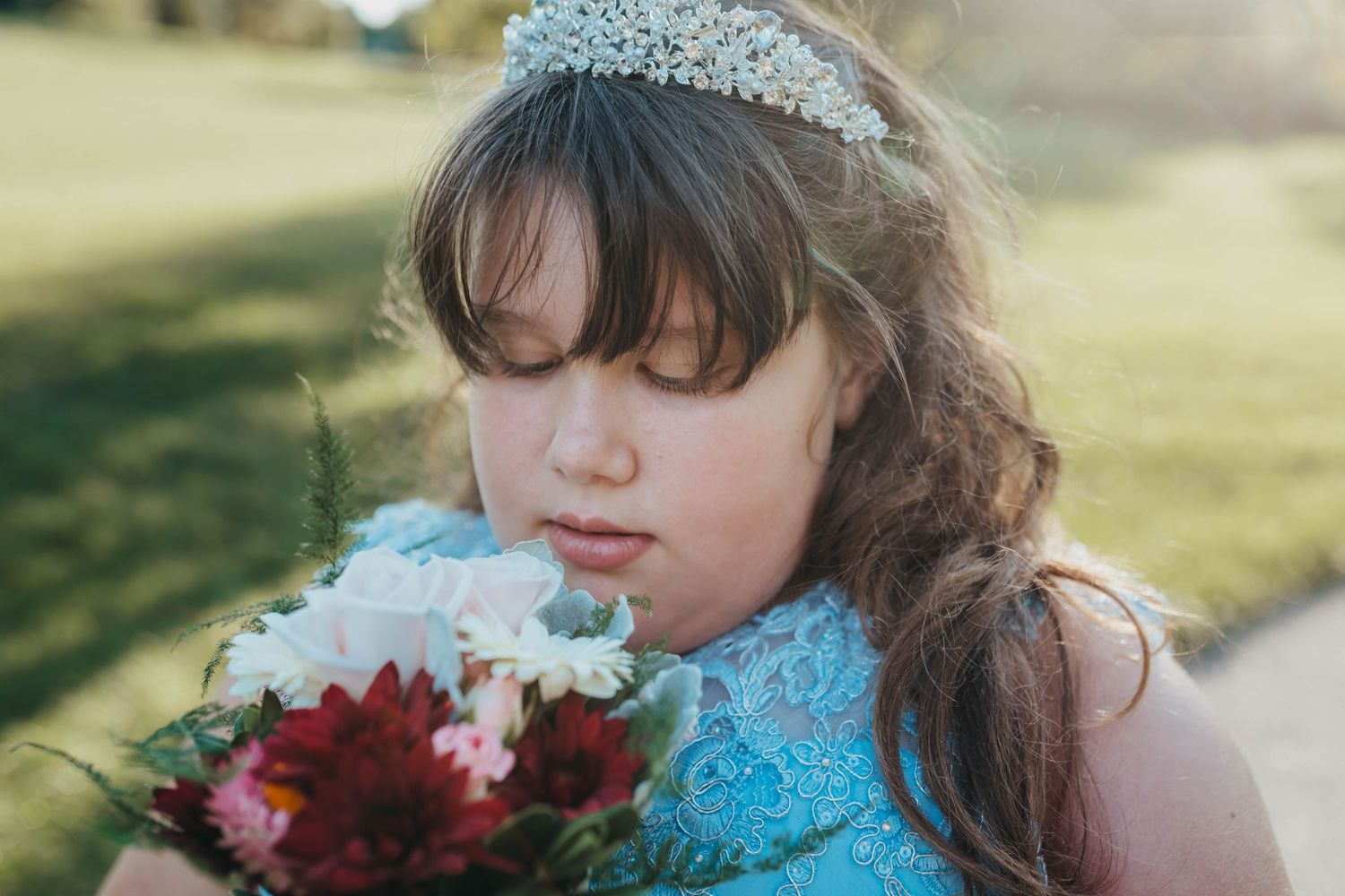 A close-up portrait of someone in a tiara holding red flowers.