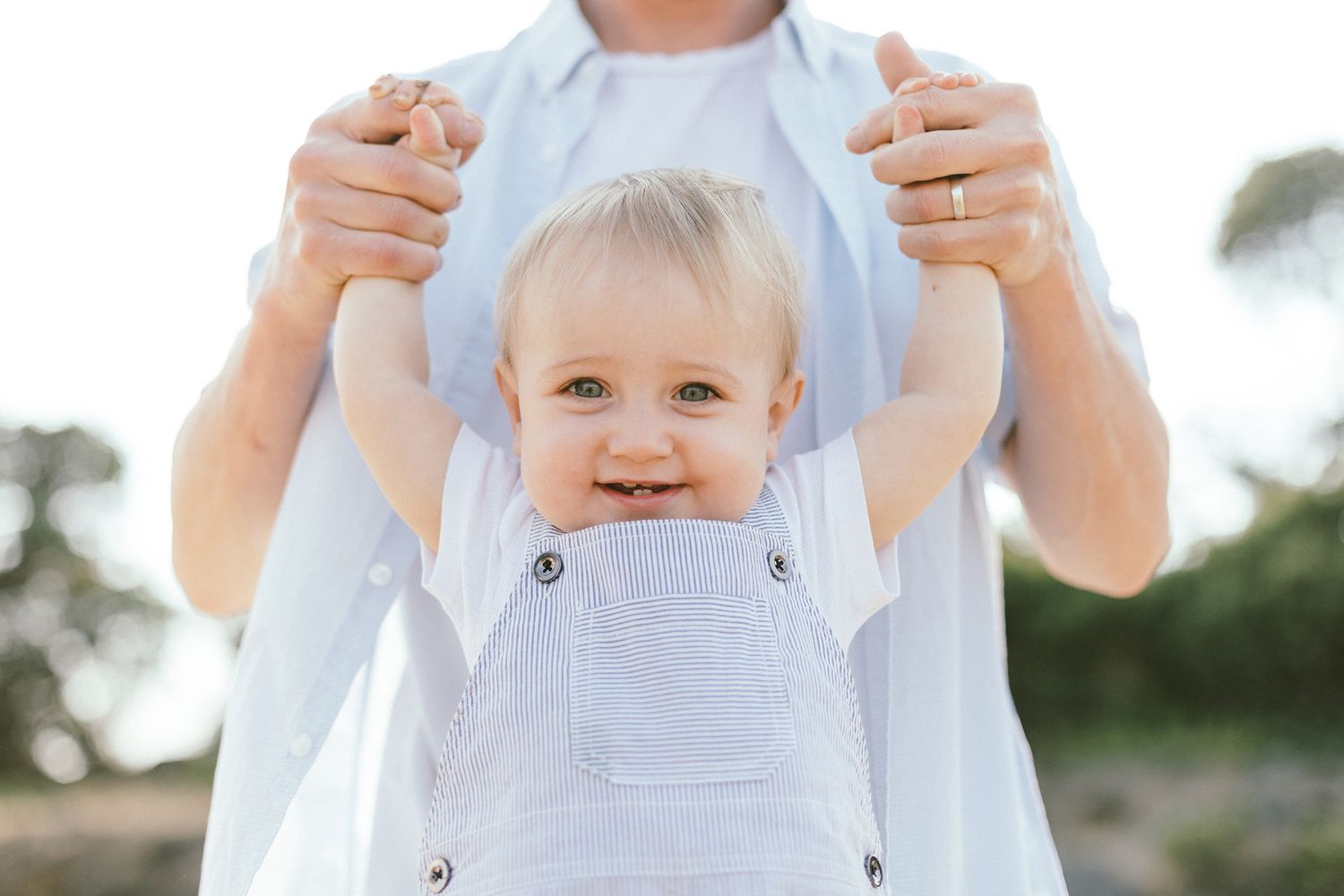 Close-up of baby in white outfit being held during beach photoshoot.