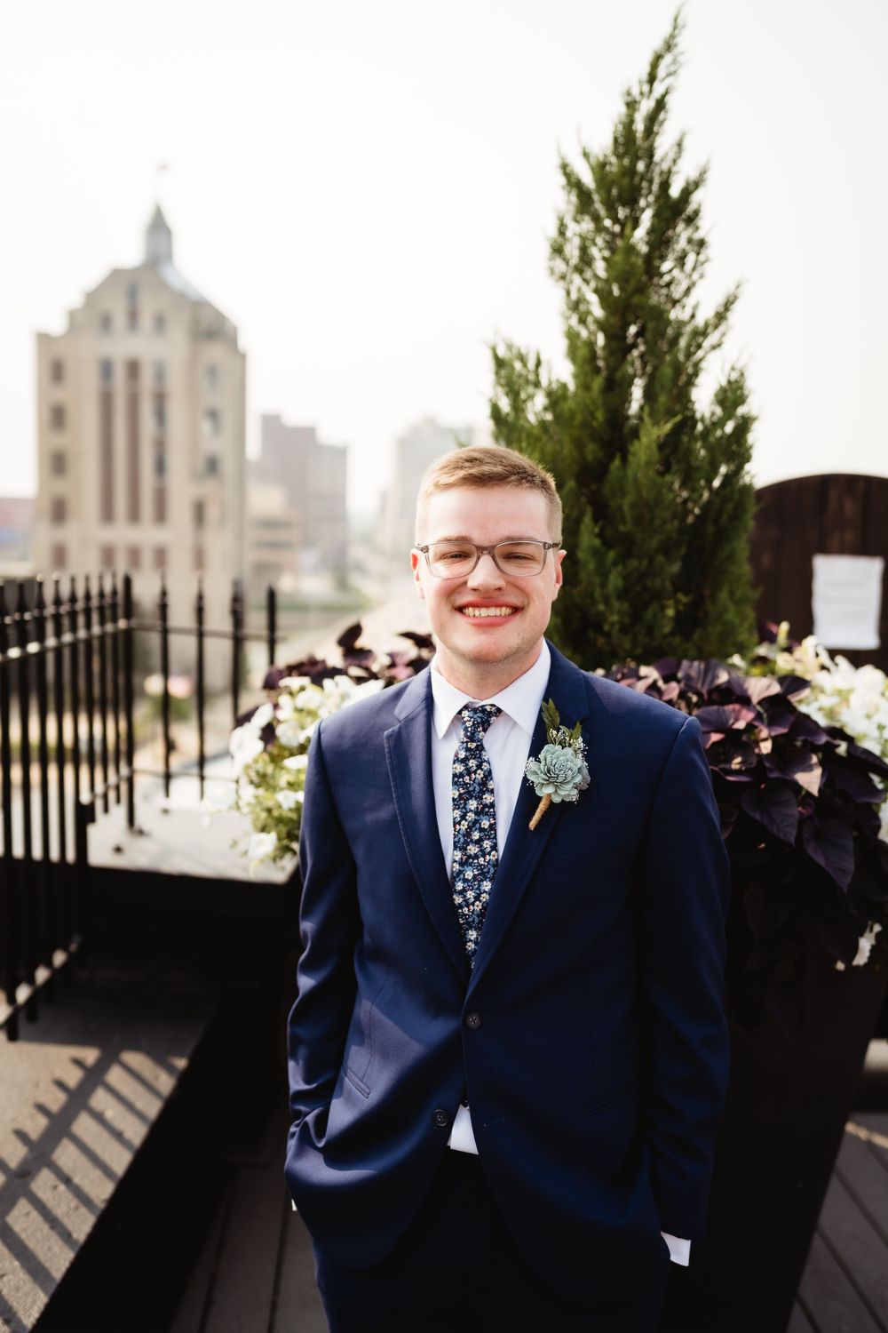 A formal wedding portrait on a rooftop terrace with greenery and city architecture in the background.