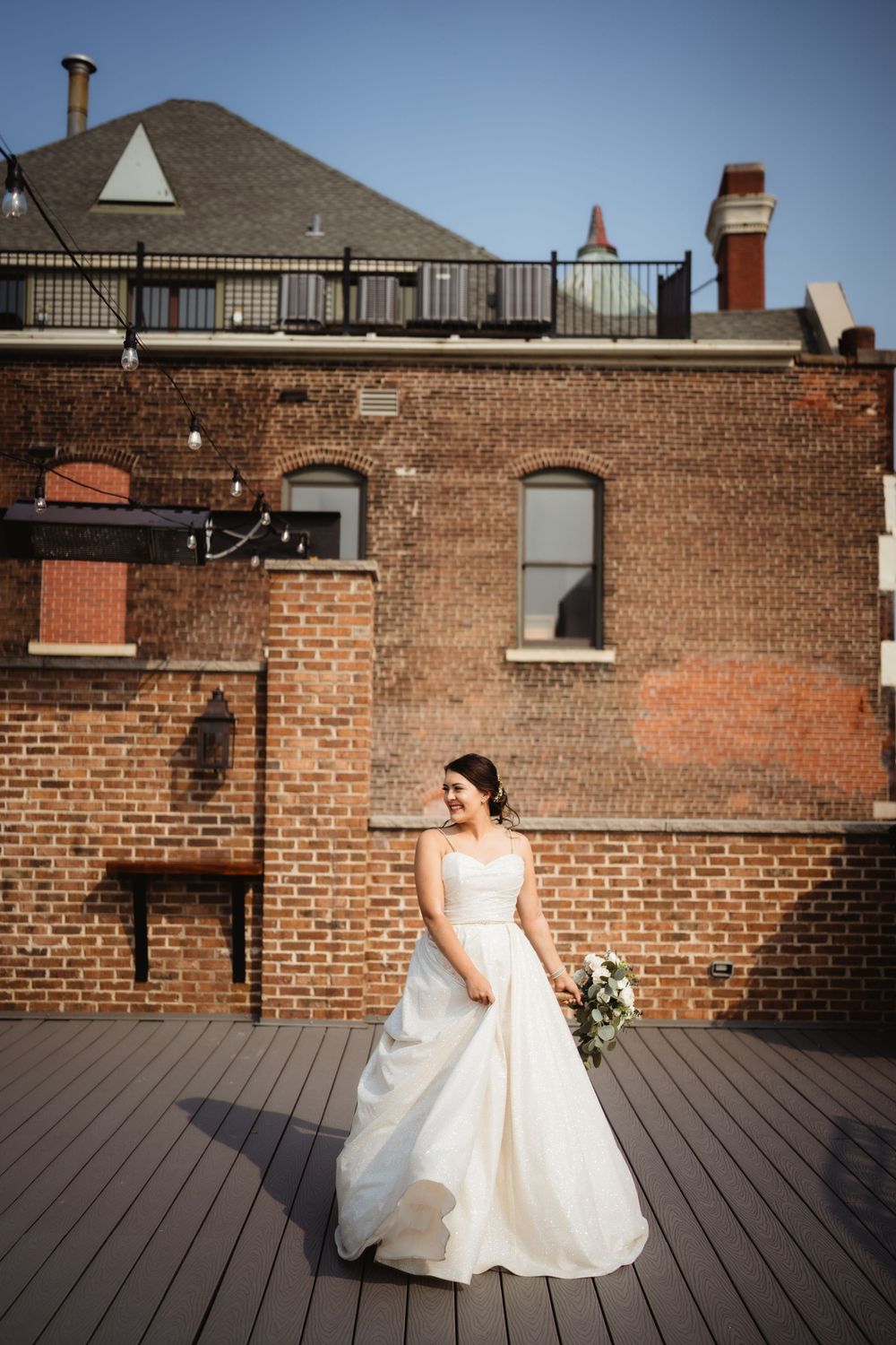 Elegant bridal portrait on rooftop deck against historic brick building backdrop.