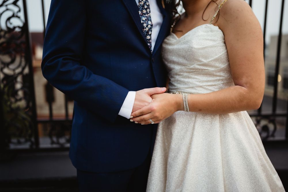 Close-up detail shot of a bride and groom holding hands, showing wedding attire in navy and white.
