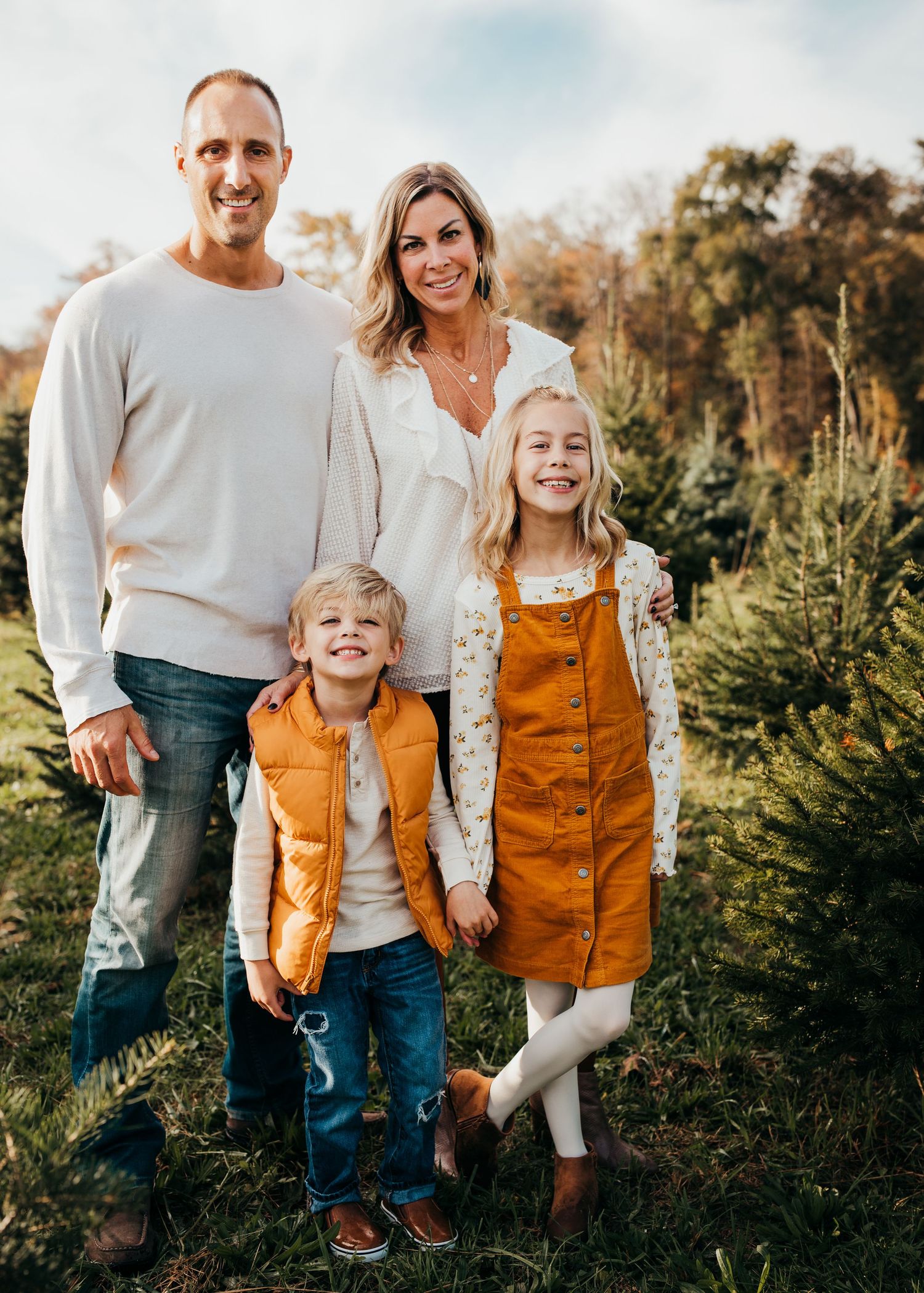 A family of four wears white and mustard color outfits for a holiday photo at Conover's tree farm.