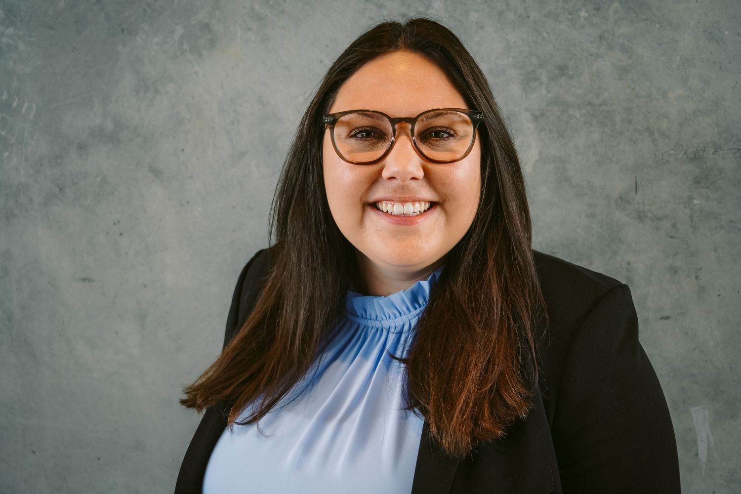 Professional headshot portrait of smiling person in business attire against gray background.