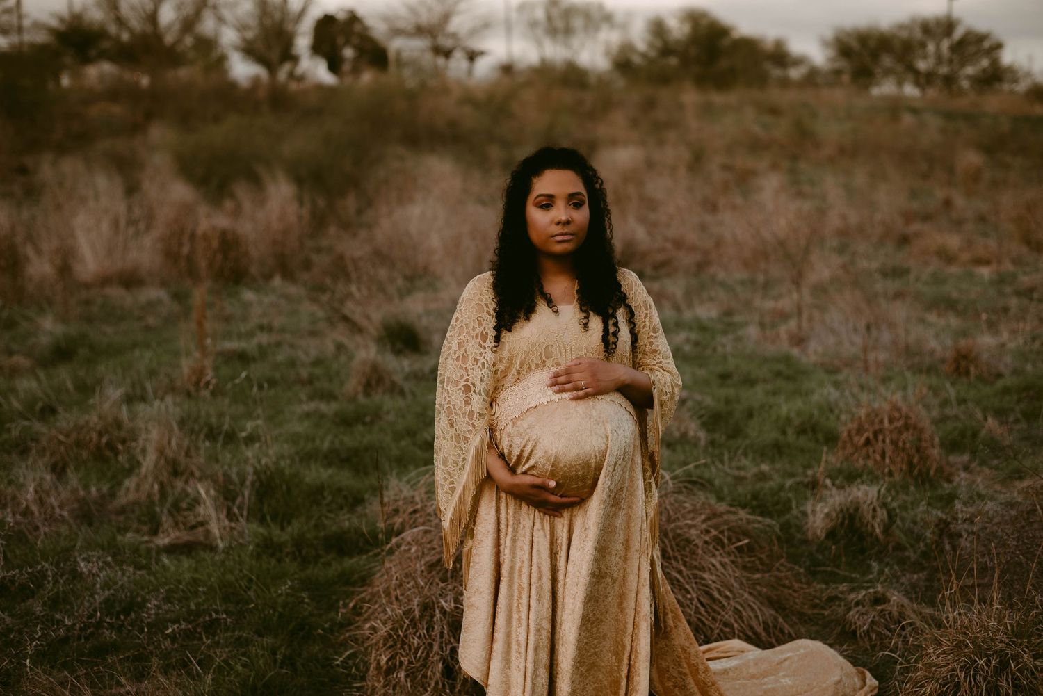 An ethereal maternity portrait captured in warm tones against a natural outdoor backdrop.