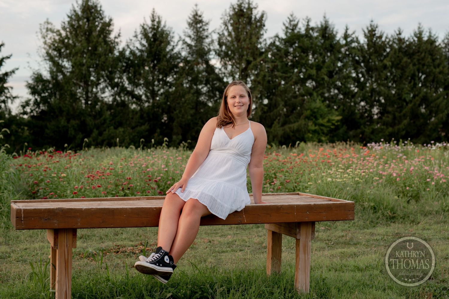 A casual summer portrait of someone sitting on a wooden bench surrounded by wildflowers.