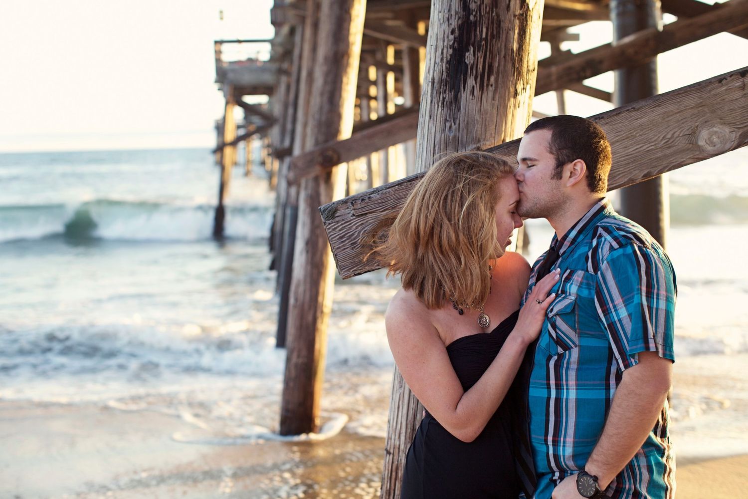 Romantic couple embracing near wooden pier at sunset by ocean.