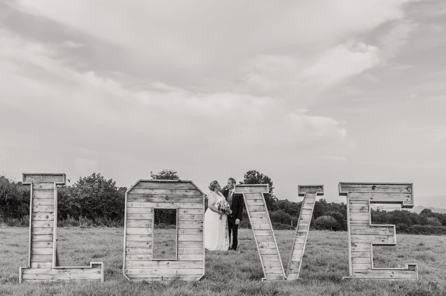 Rustic wooden LOVE letters displayed outdoors against cloudy sky.