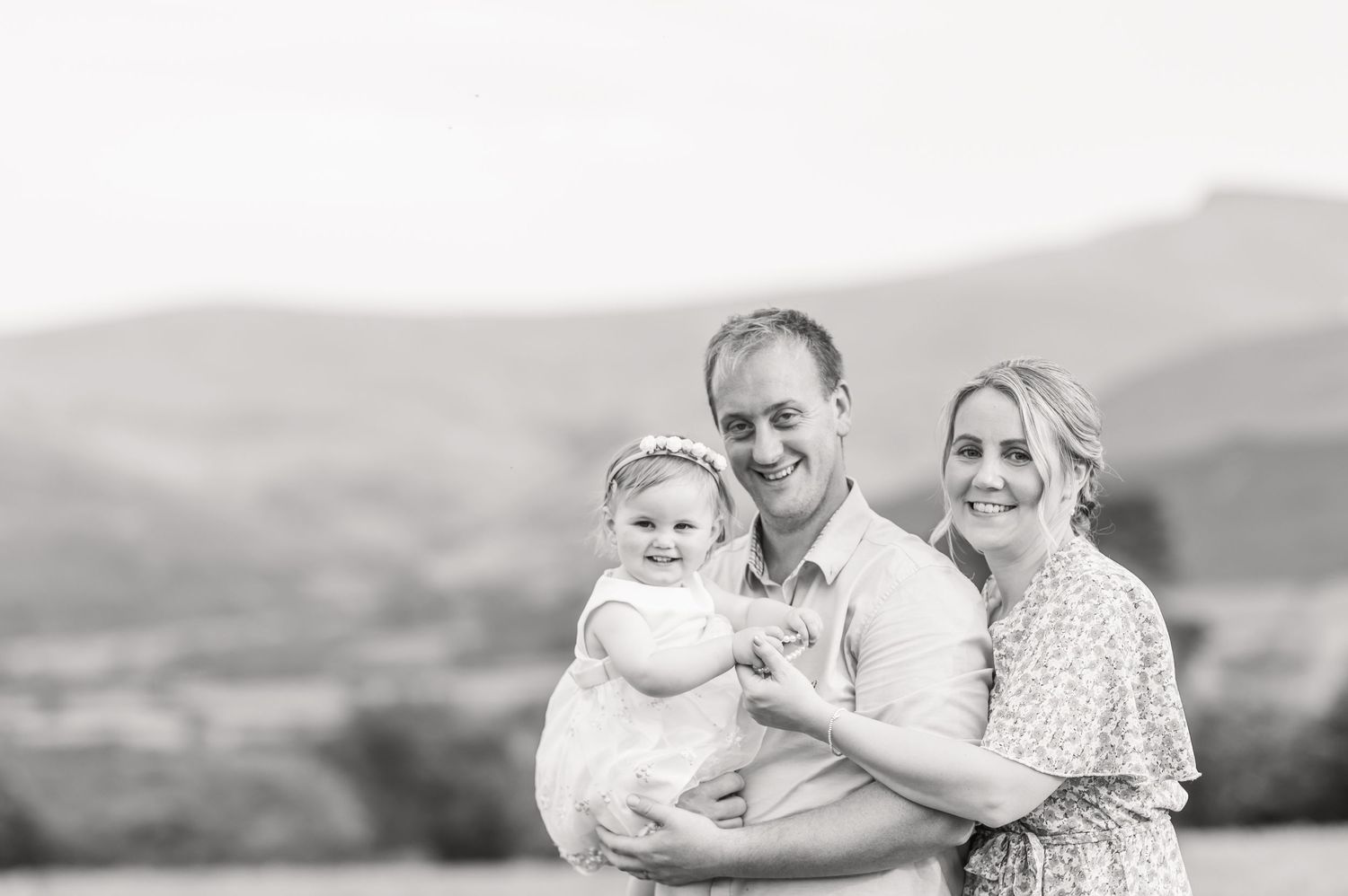 A couple poses in a scenic outdoor setting while holding their young child during a family photo session.