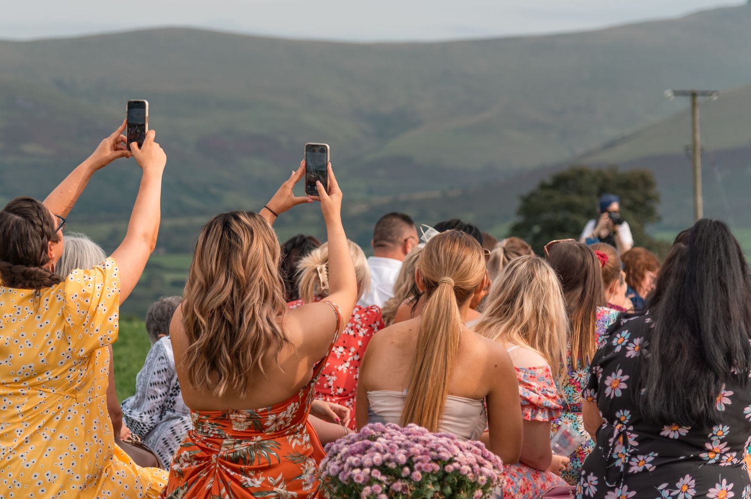 Wedding guests taking photos of scenic mountain views at outdoor celebration.
