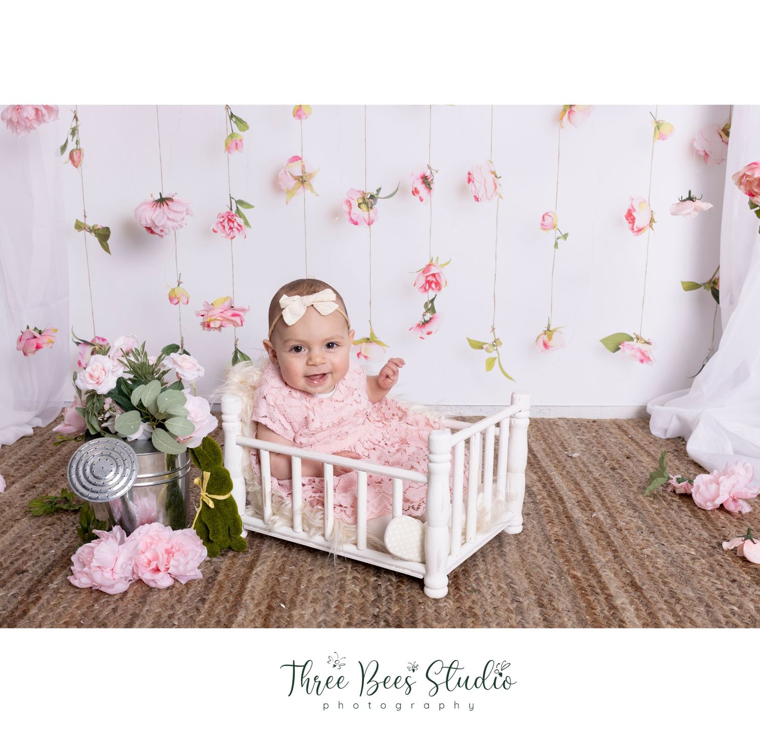 Baby photography setup with white crib and delicate pink floral wall decorations.